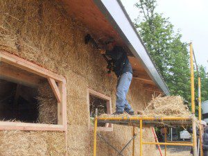 man smoothing straw bale house wall