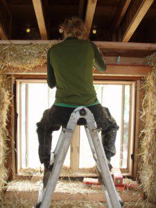 Woman on ladder working on straw bale house