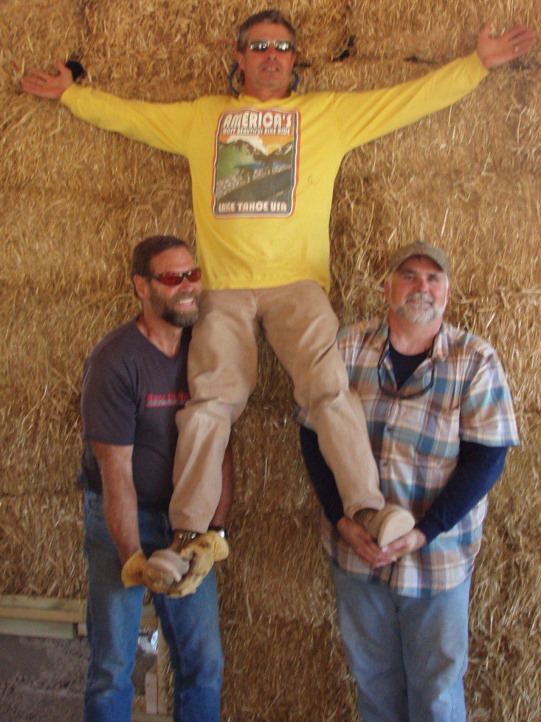 three men standing on straw bale wall