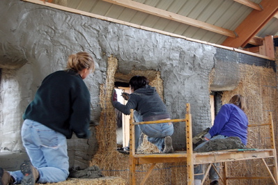 people plastering a straw bale house